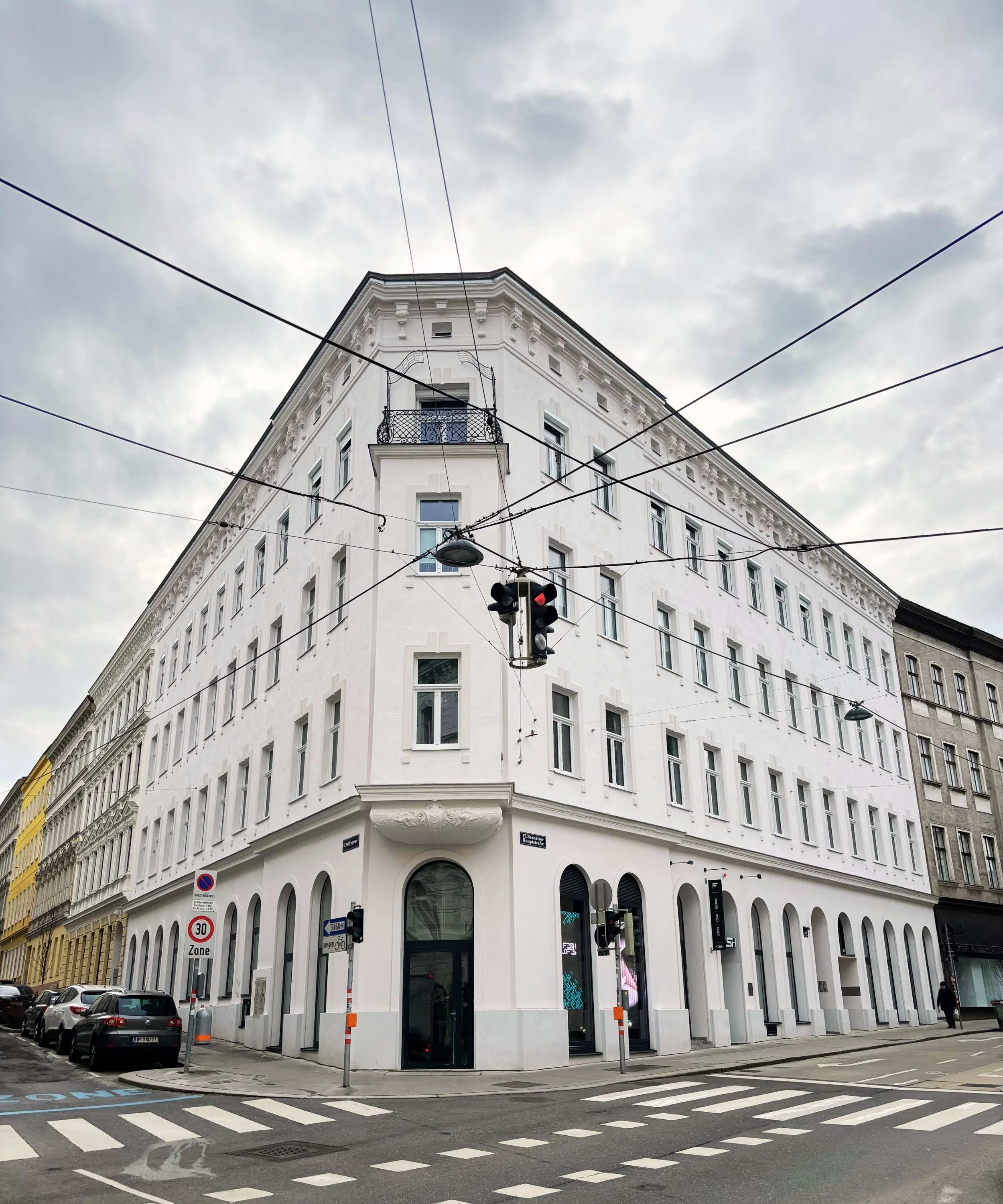 A white multi-story building with arched windows on the ground floor, situated on a city street corner.