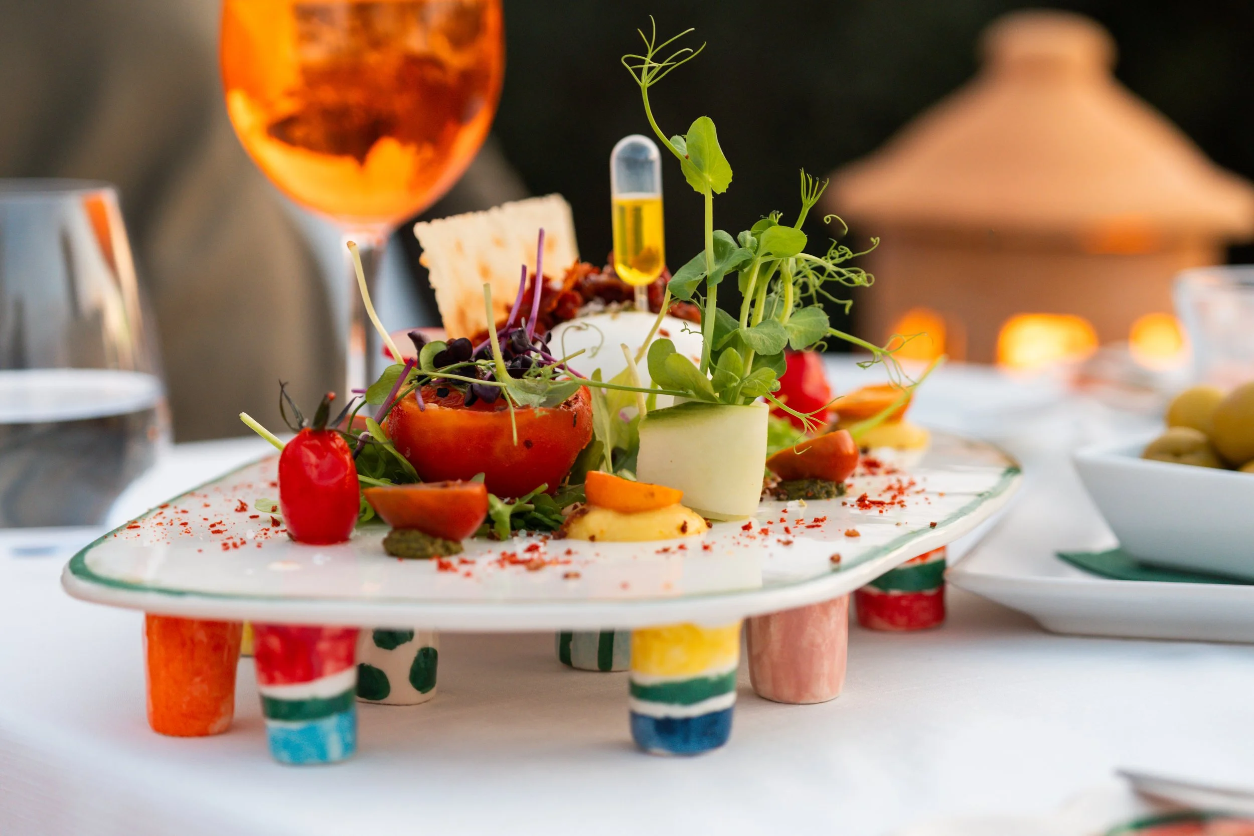 Plato de comida gourmet con vegetales, un huevo, y una pipeta con líquido amarillo en una mesa elegante.