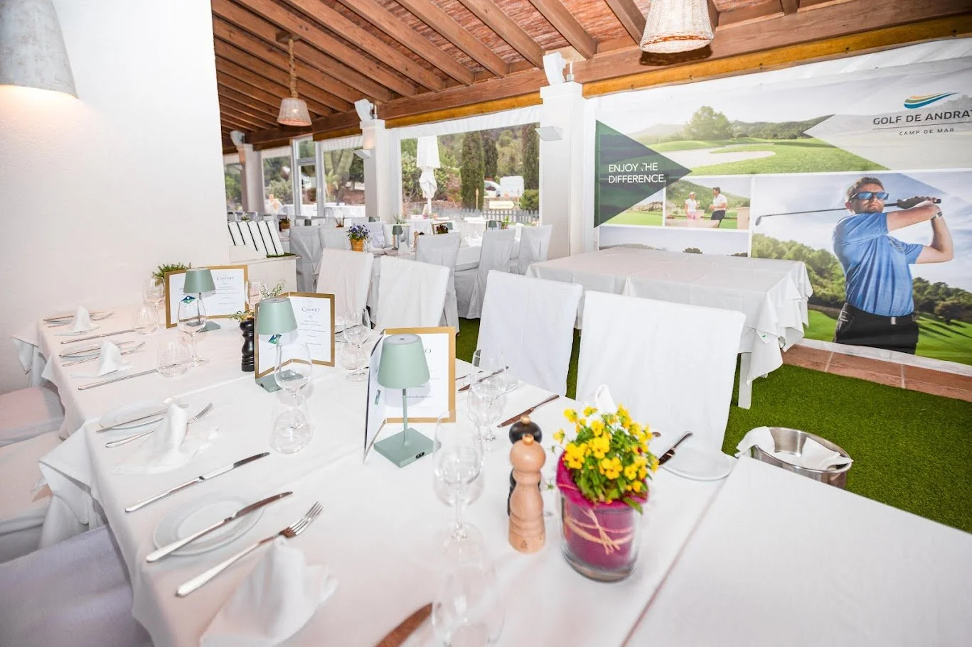 Sala de eventos decorada con mesas y sillas blancas, con un ambiente elegante y vistas a un campo de golf.