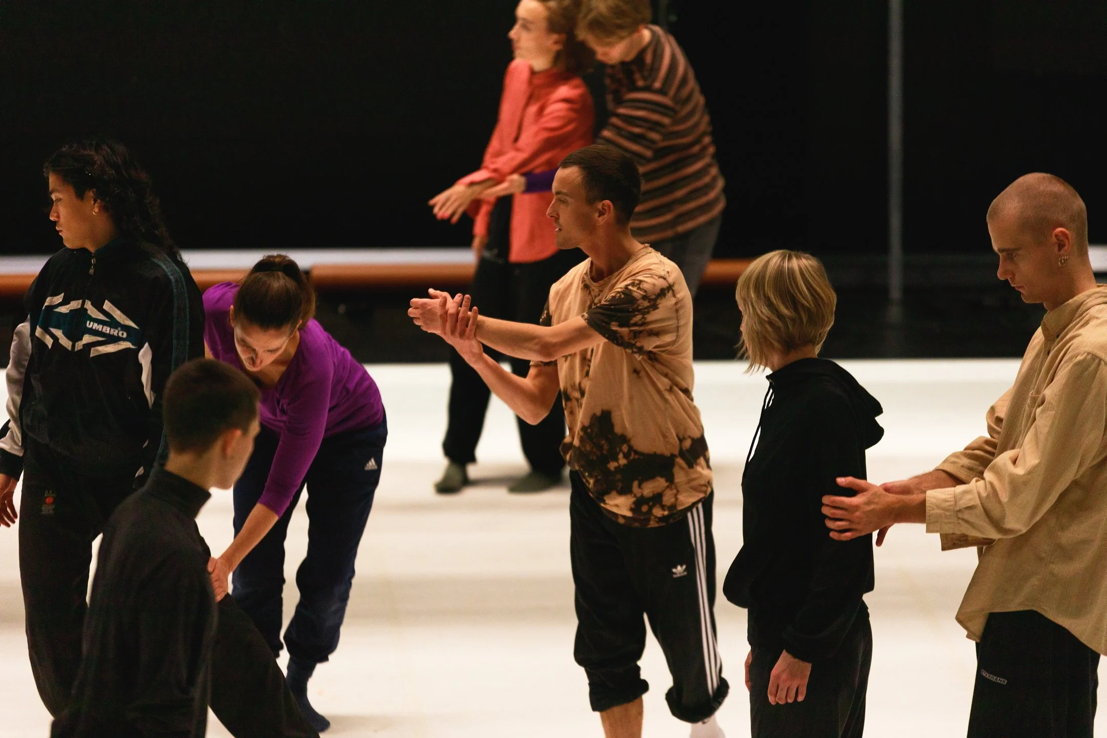 Flere personer deltar i en danseworkshop på lyst gulv, i ulike bevegelser og posisjoner.