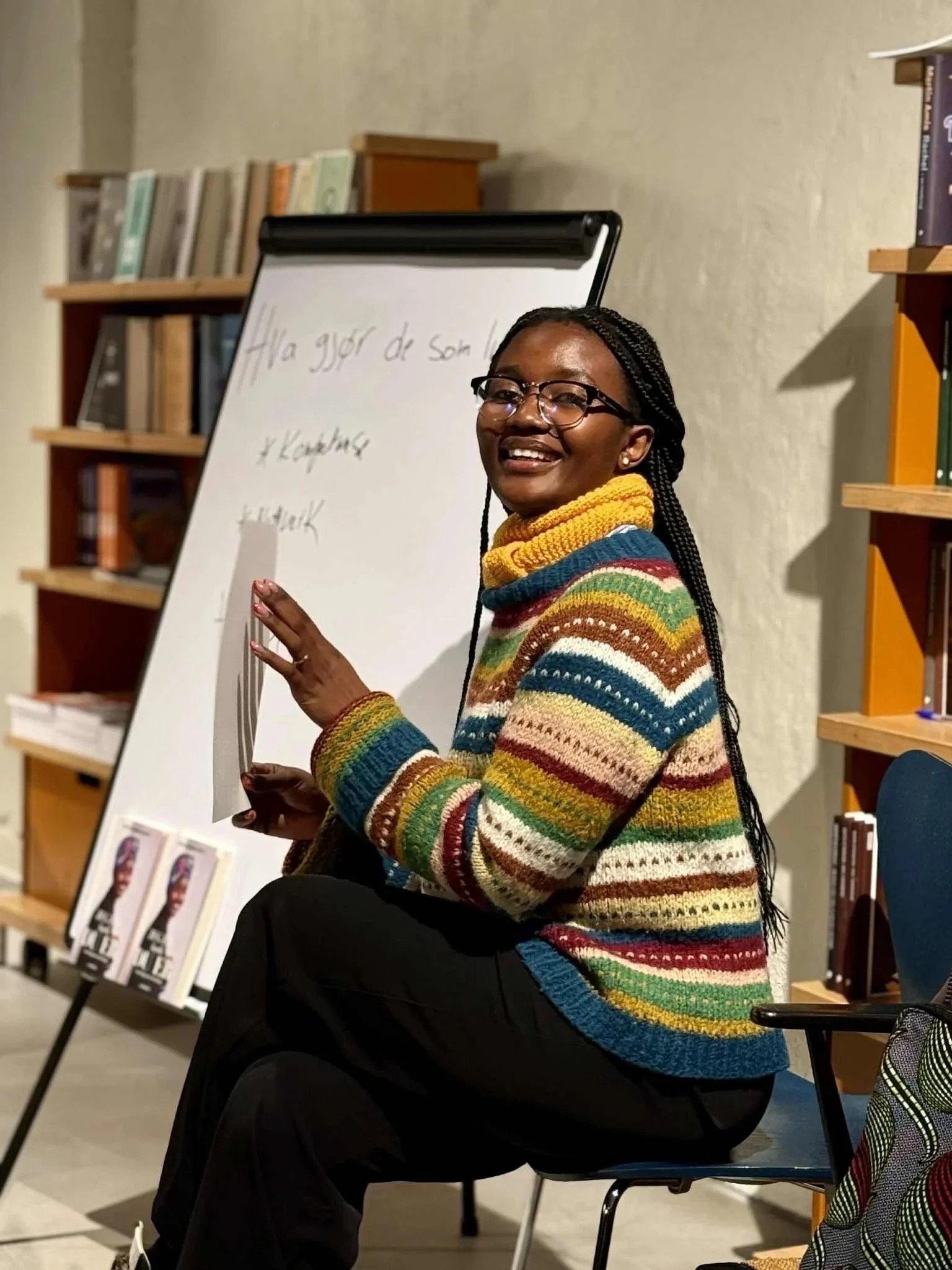 Irene Afriye sitter på en stol med et ark i hendene og smiler til kamera