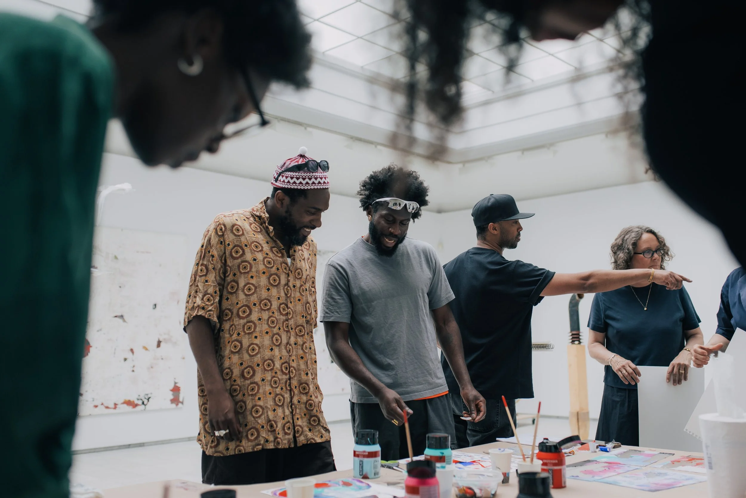 En gruppe mennesker står rundt et bord med maling og kunstmateriell i et lyst atelier.