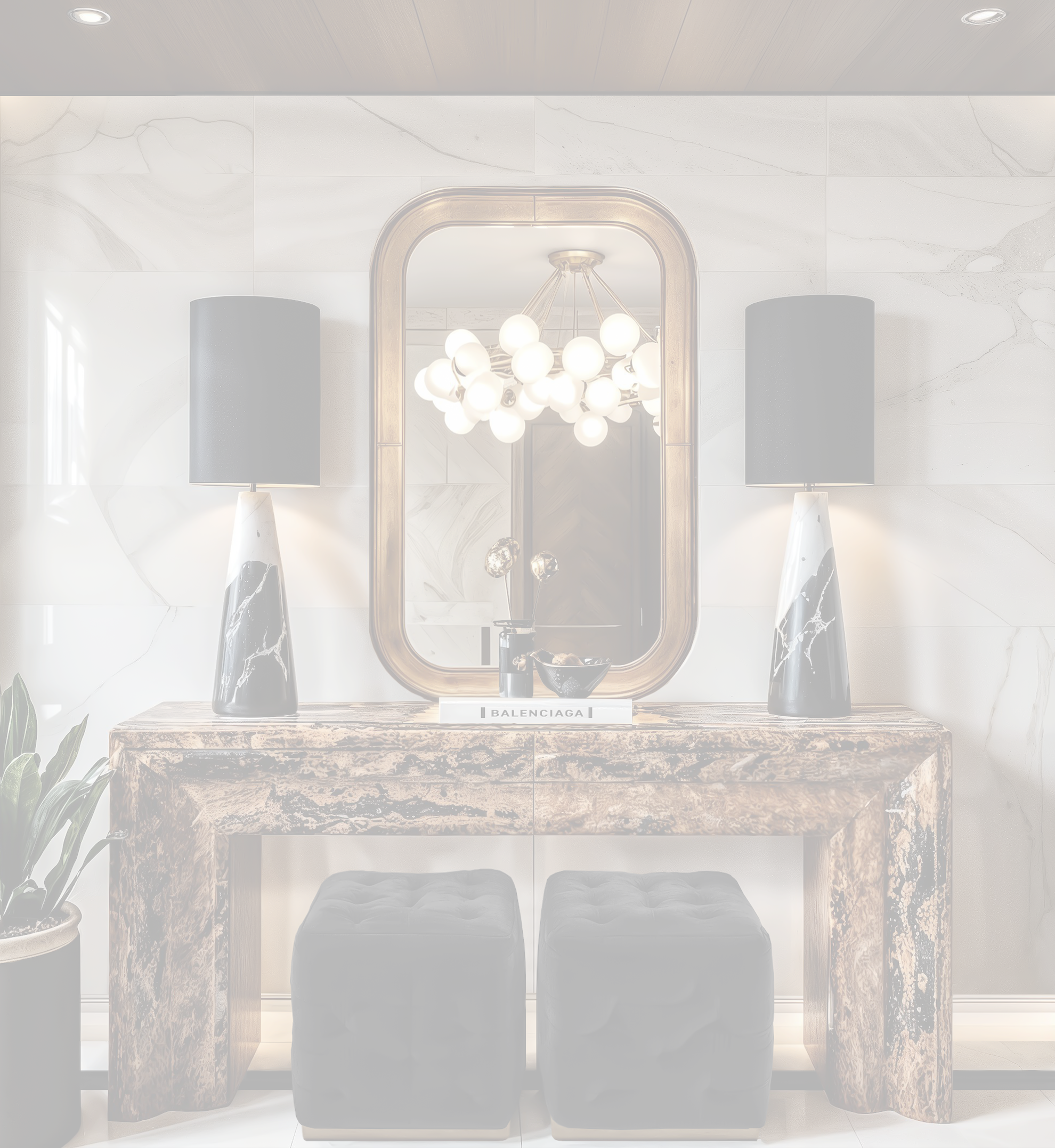 A modern hallway console table with two black and white marble lamps, a mirror, a chandelier, and a plant on the left. Items on the table include a black bowl and a book labeled "Balenciaga."