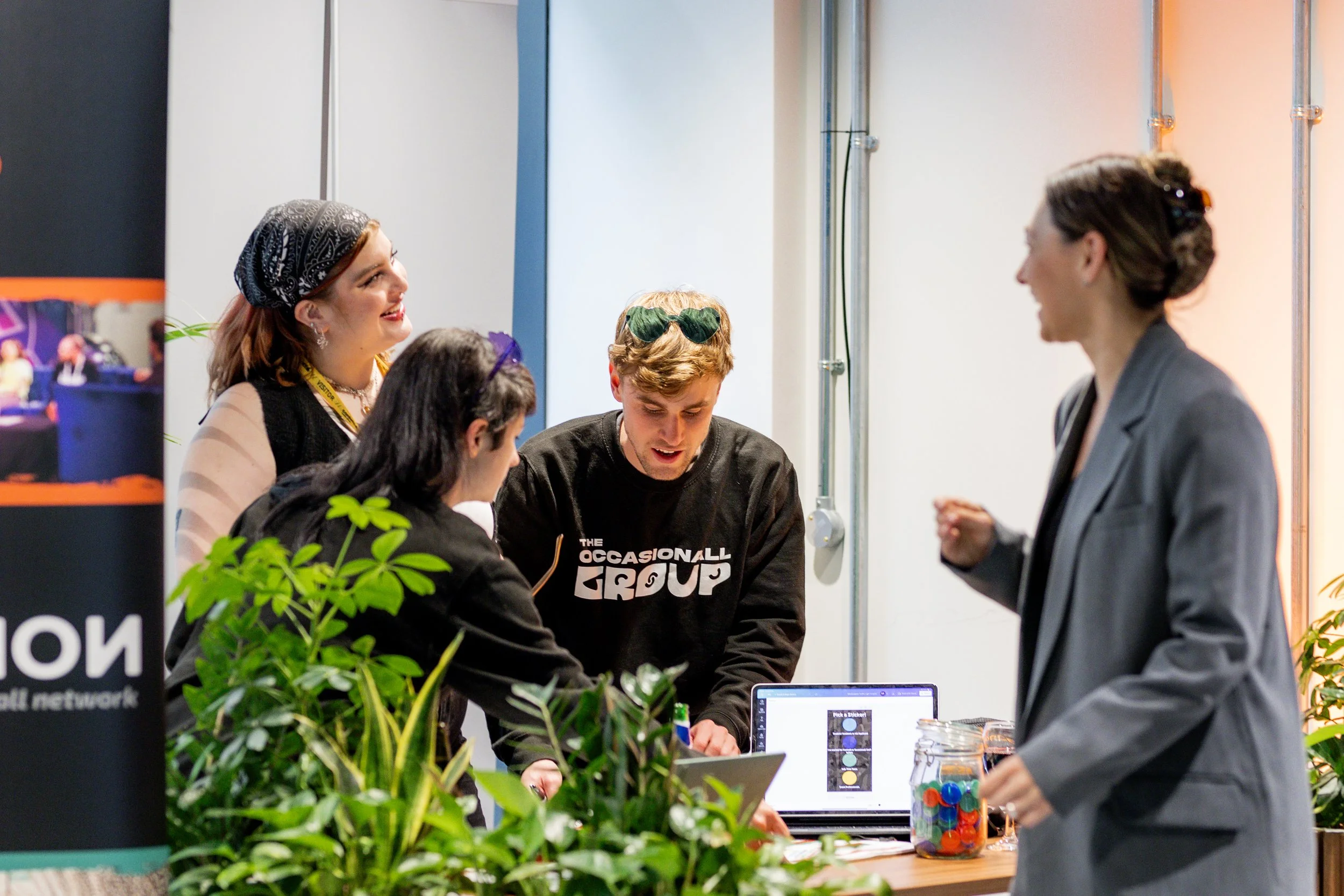 Group of people collaborating around a table with laptops and plants.