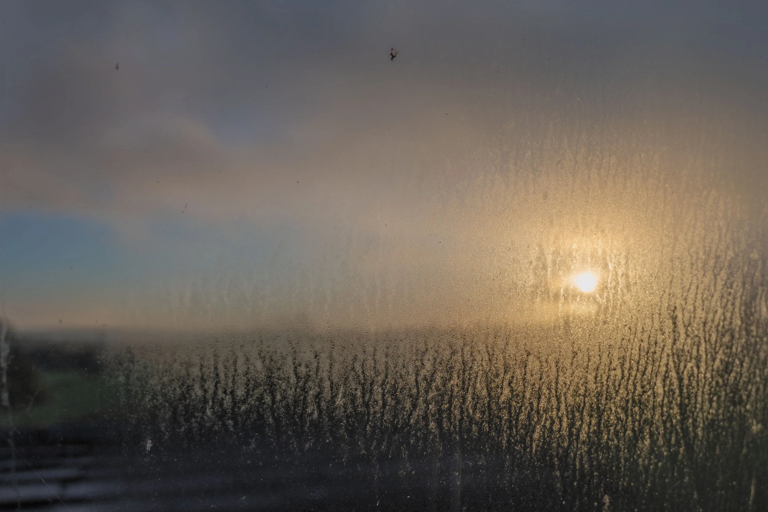 Uitzicht op zonsondergang of zonsopgang gezien door een raampaneel beslagen met koude druppels op het glas.