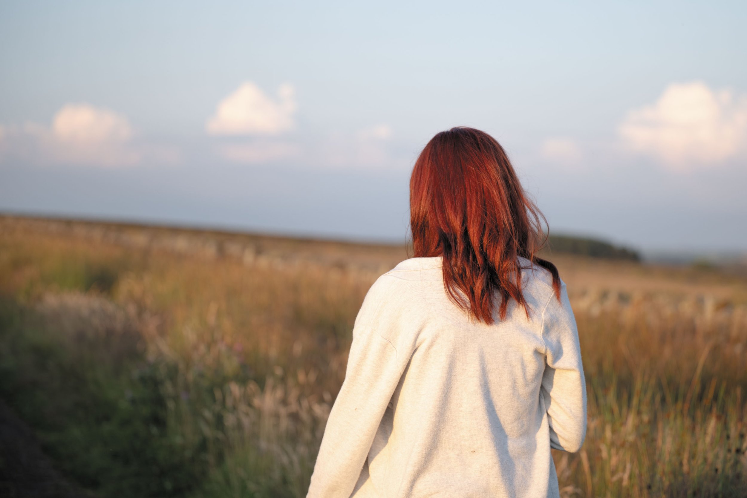 Vrouw met rood haar die in een veld staat, naar de lucht kijkt.