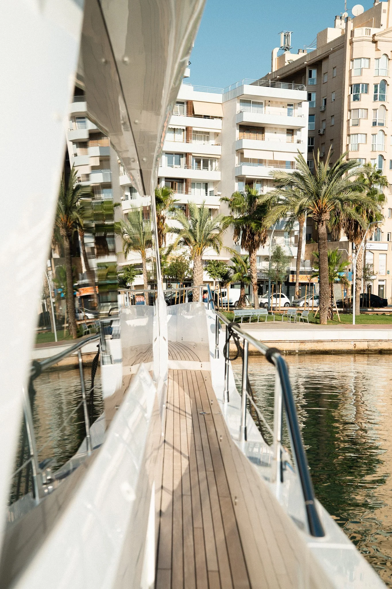 View from a boat showing a dockside with palm trees, modern apartments, and a waterfront promenade in a sunny location.