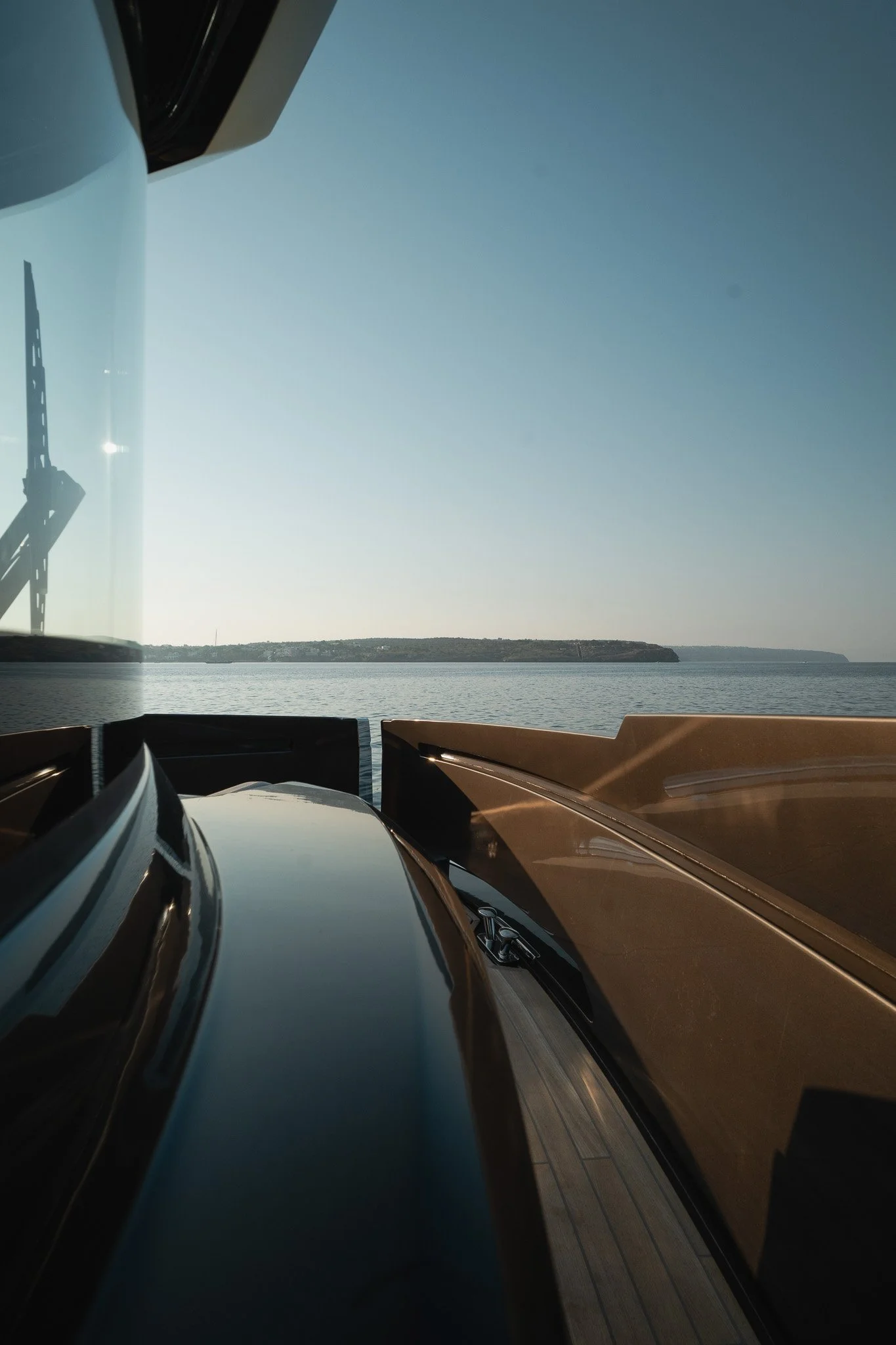 View from a boat with water and land in the distance, showing the boat's glossy black and brown surfaces, and a clear blue sky.