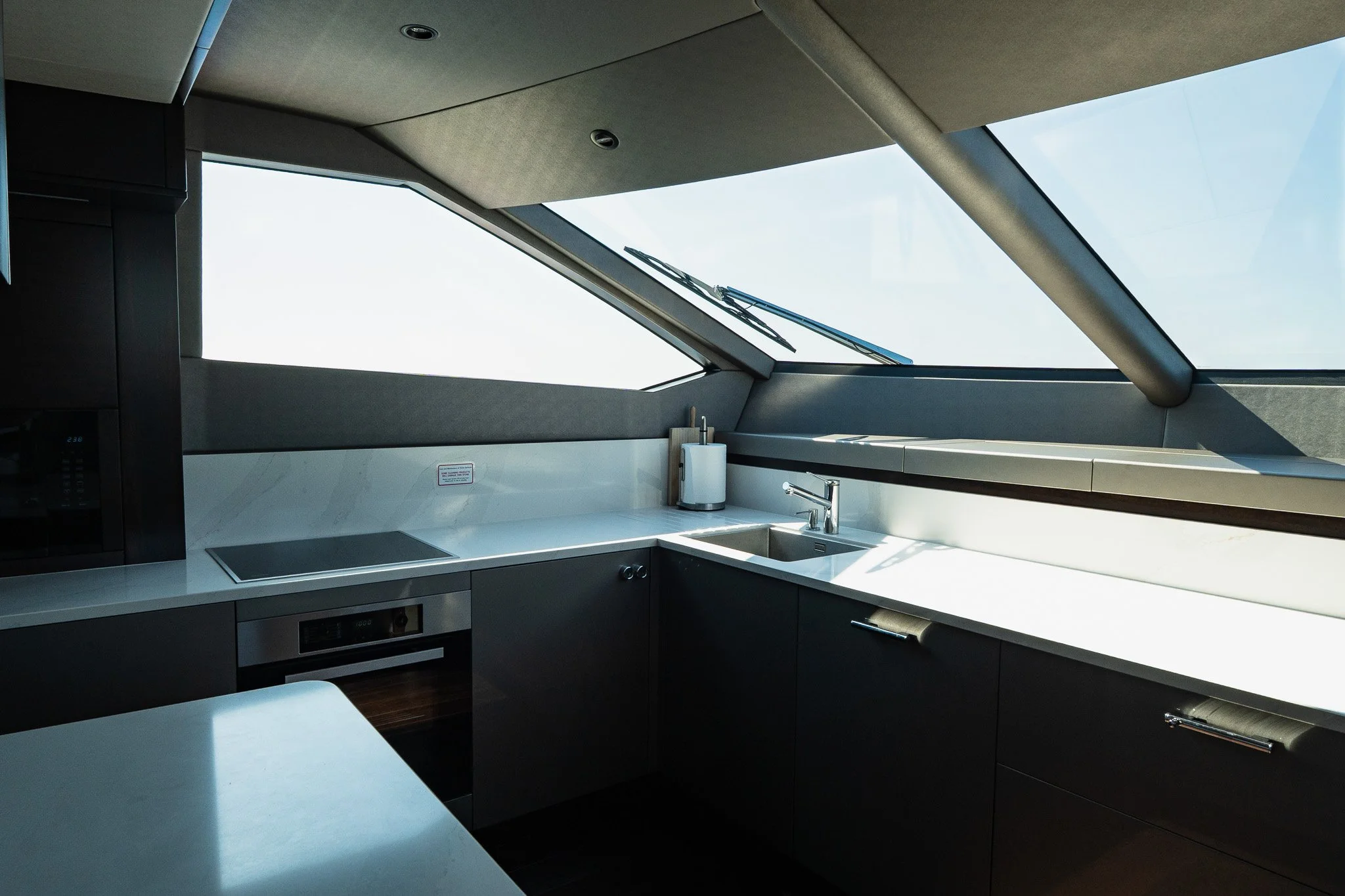 Modern kitchen with white countertops, black cabinets, a sink, paper towel holder, on a slanted windowed ceiling.