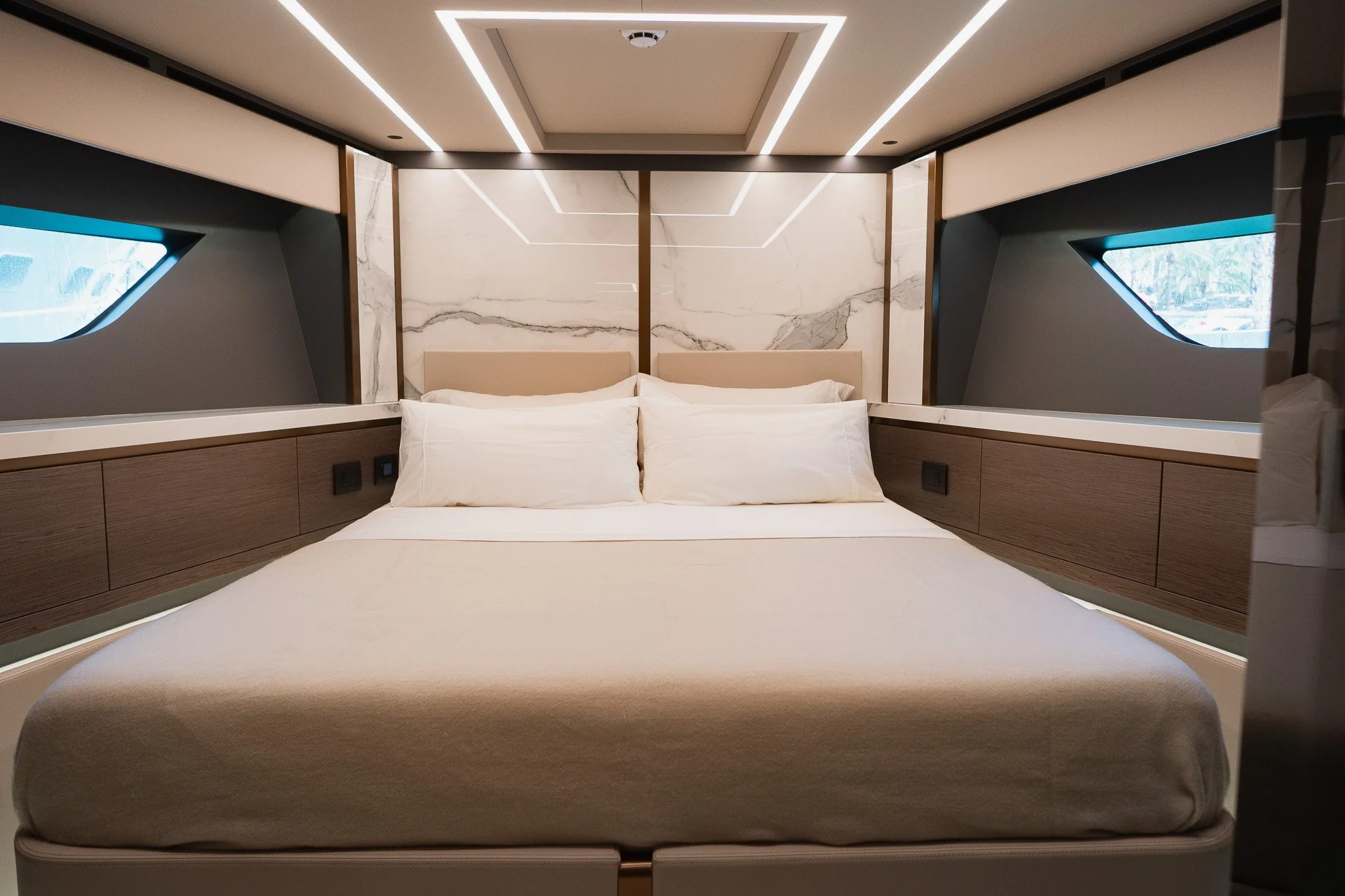 Modern bedroom with a double bed, white bedding, and two pillows, flanked by wooden paneling and geometric wall features with windows on adjacent sides.