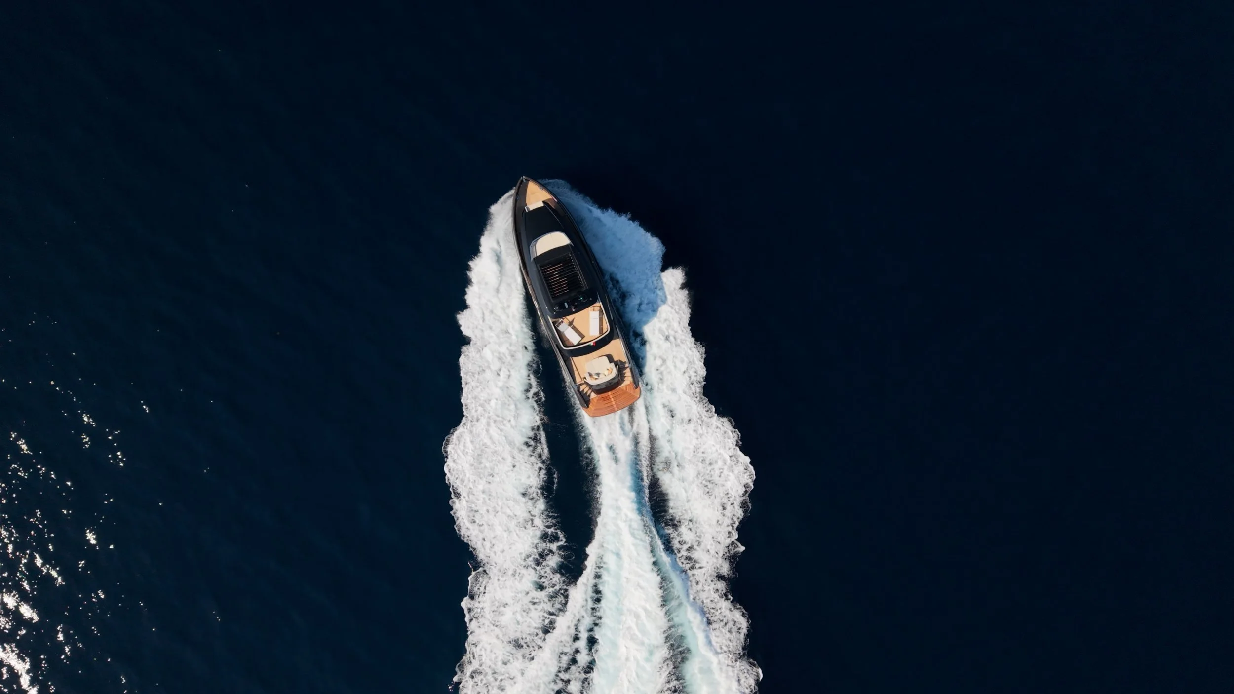 Aerial view of a motorboat moving fast through dark blue water, creating white wake behind it.