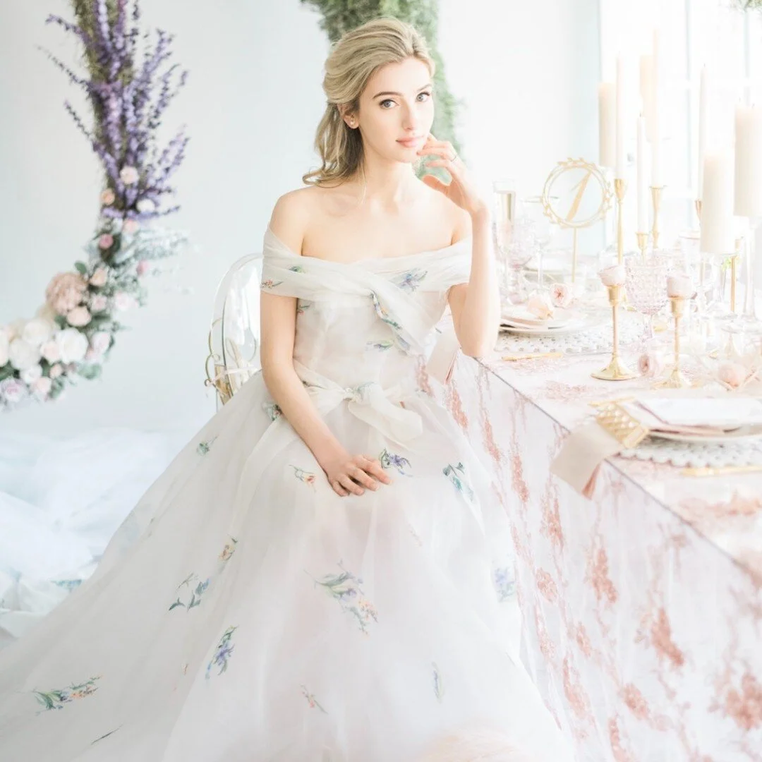 This tablescape is meticulously arranged with tall candles, delicate glassware, and ornate dinnerware. An arch decorated with greenery and soft purple flowers frames the background, enhancing the romantic and opulent ambiance. #tablescape #wedding #d