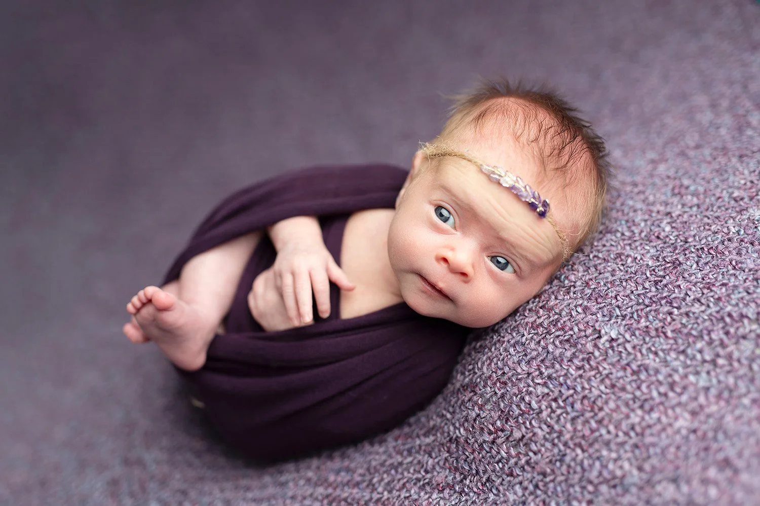 awake newborn girl on purple