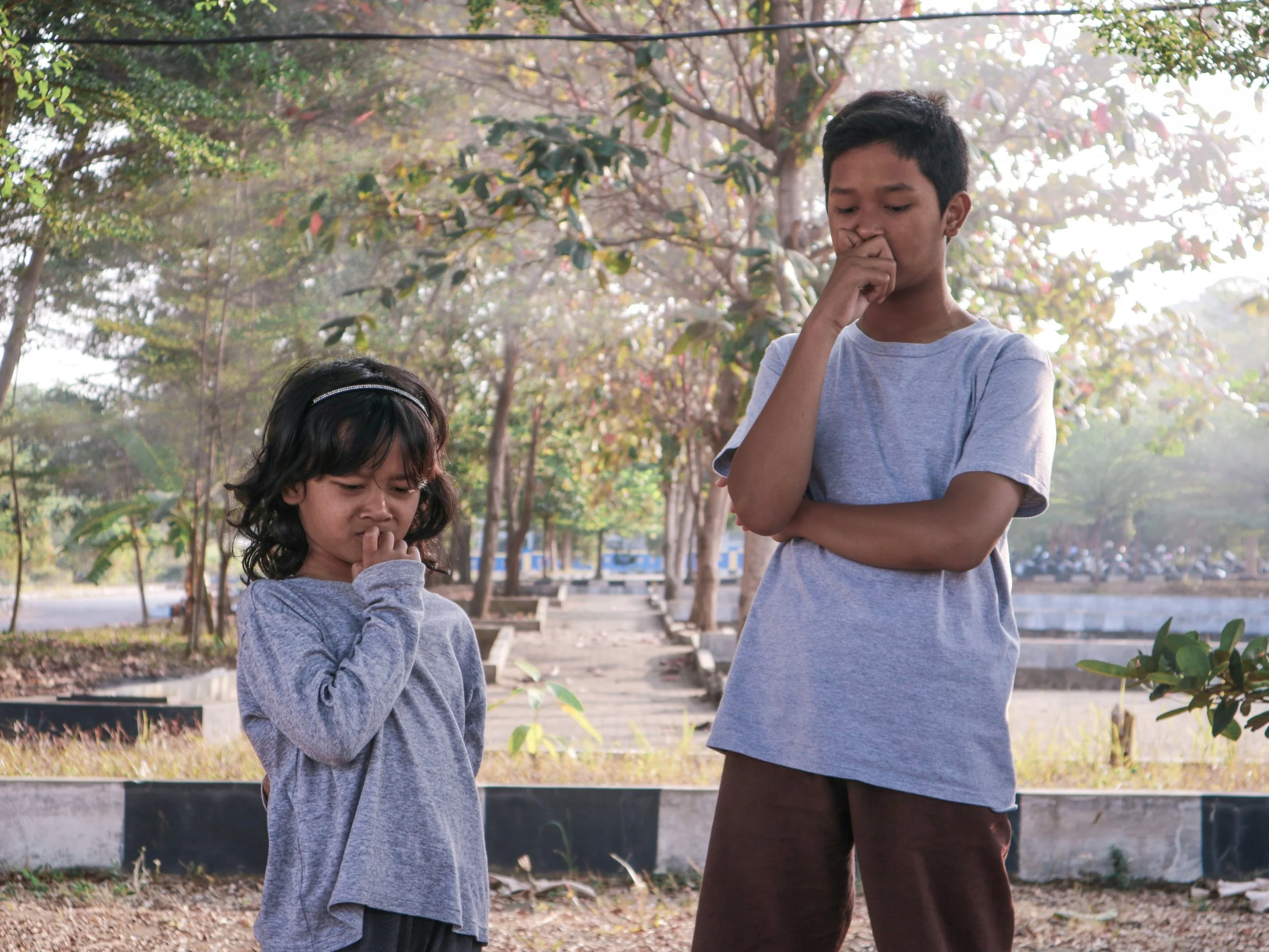 Brother and sister standing outside looking contemplative.