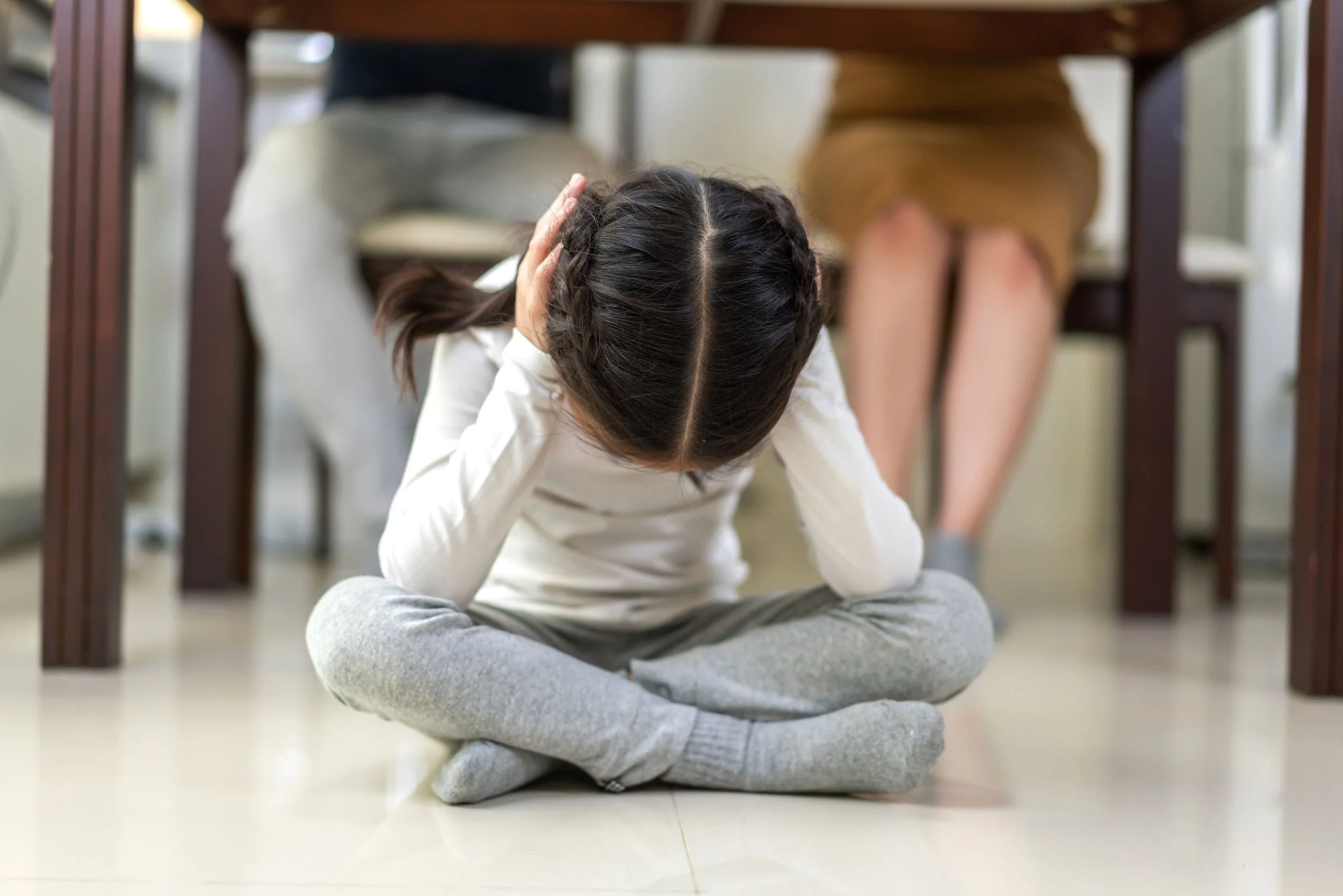 Young girl covering her ears sitting under the table.