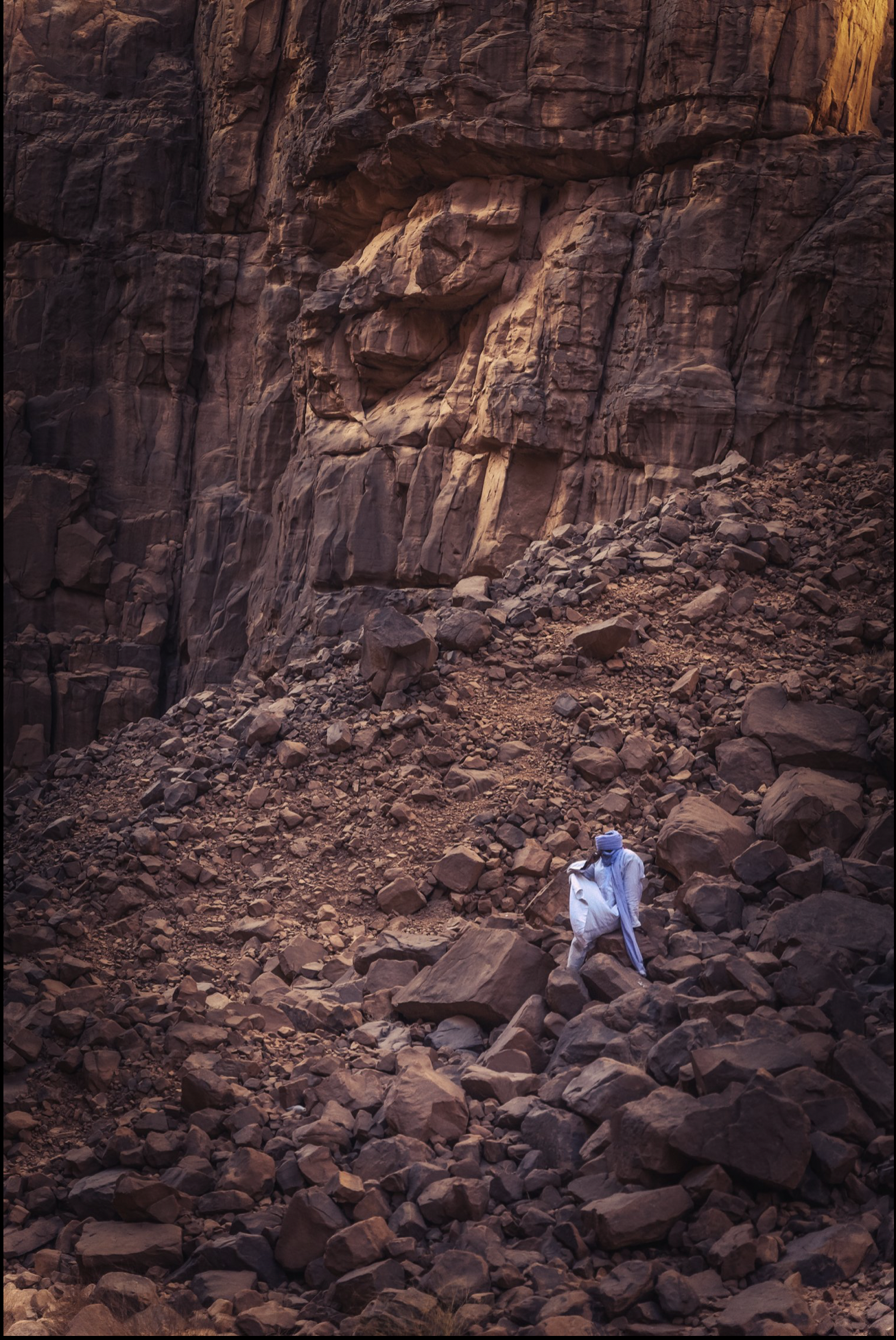 Kel Ténéré — Those of the desert
Leonardo Antonio Avezzano
[2023, 70X100]
Mohamed emerges in the canyon wearing a white robe and a sky-blue chèche, a luminous presence framed by the rock walls of the Tassili.
These natural passages lead up to the pla