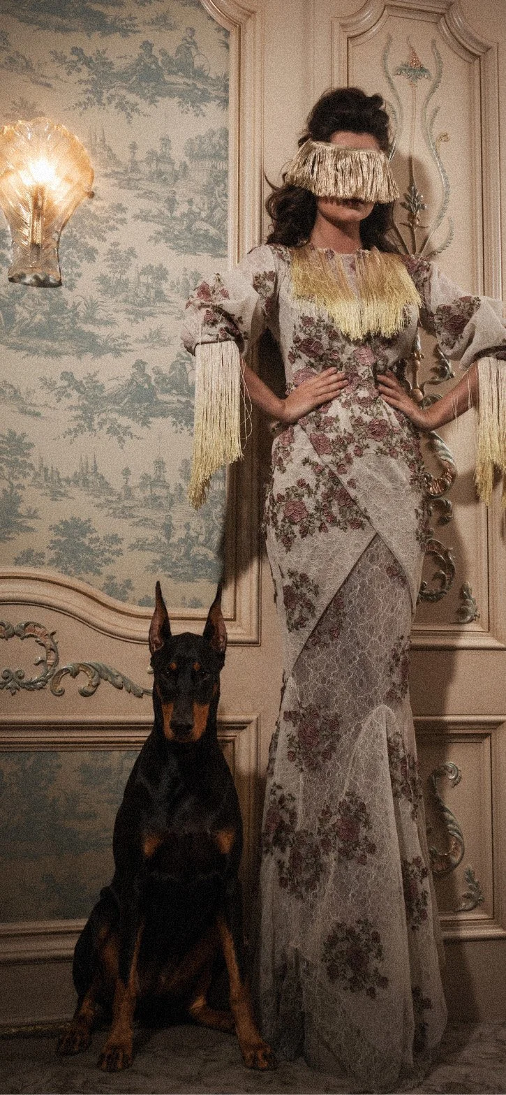Persephone the Doberman next to a woman in a vintage dress in front of a chinoiserie wallpaper and wood paneled wall