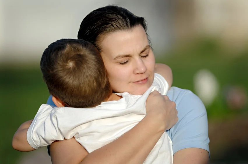 Woman hugging a young child outdoors with a blurred green background