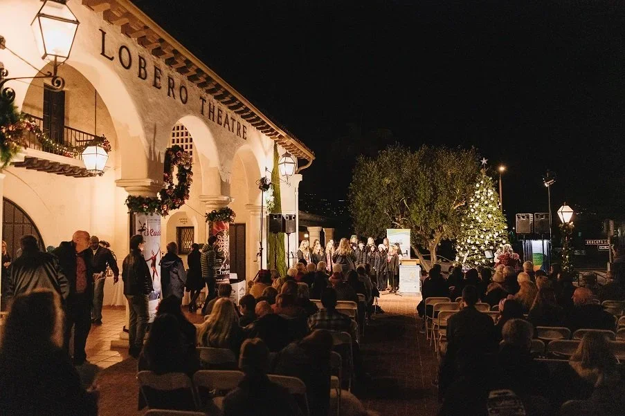 Nighttime outdoor performance at Lobero Theatre with audience seated, musicians and performers on stage, and decorated Christmas tree.