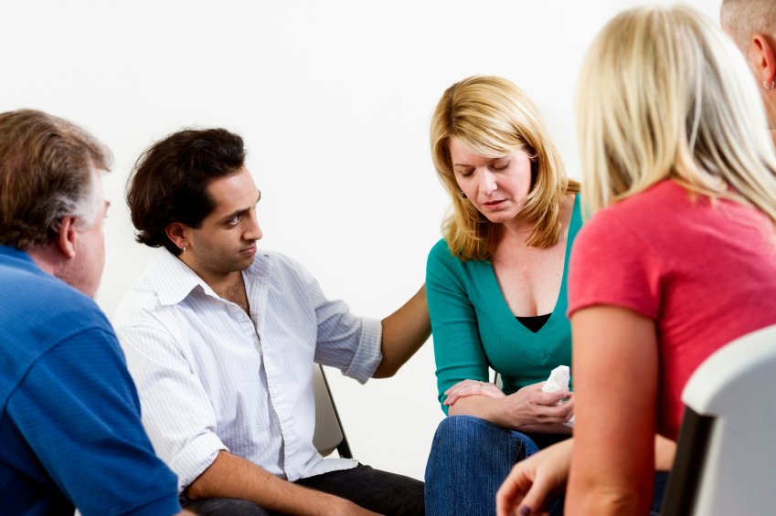 A woman with blonde hair appears upset or emotional during a group therapy or support group session with three other people.