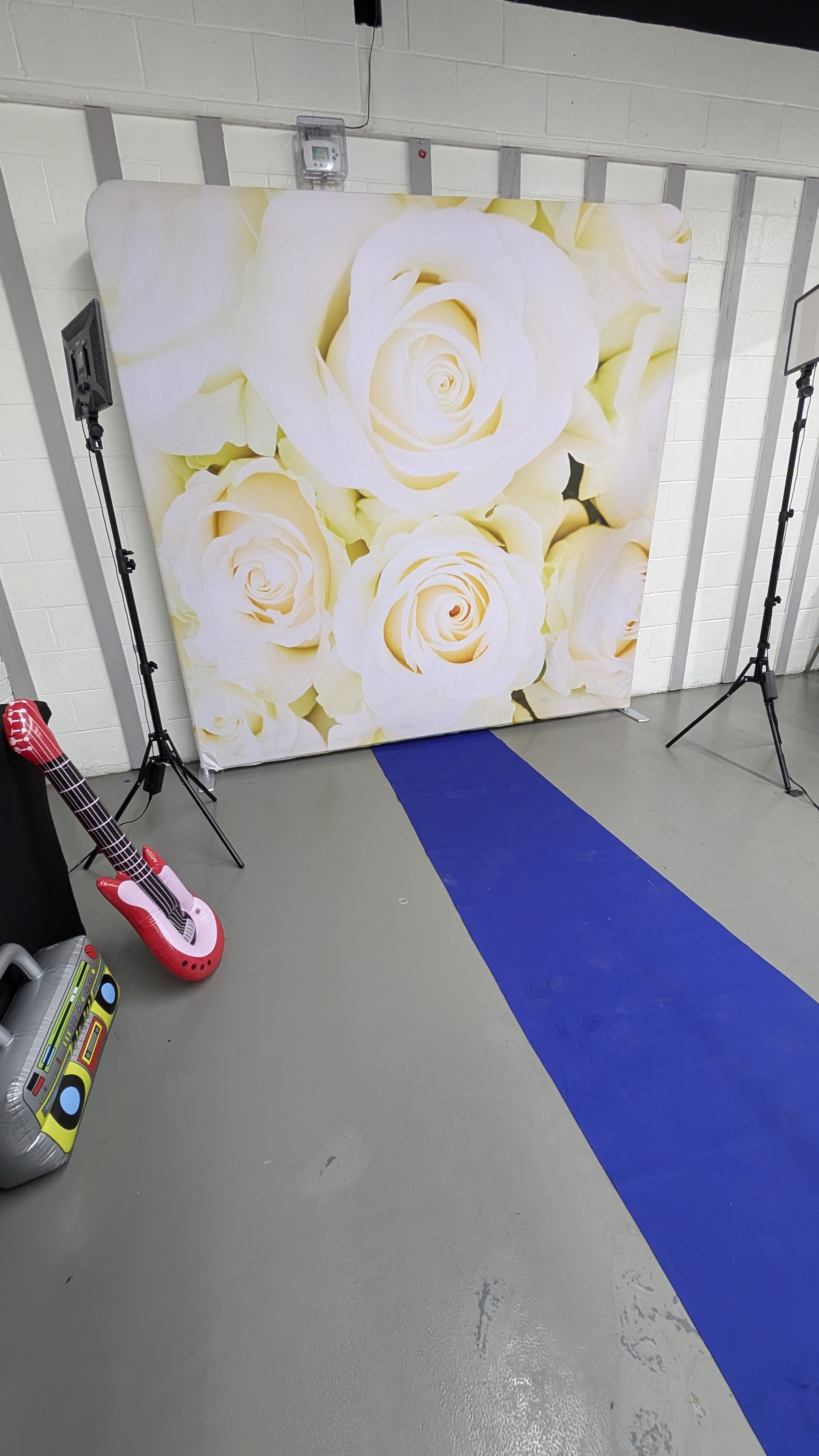 Backdrop featuring large white roses, set up with two tripod lights in a room with white brick walls and grey floor.