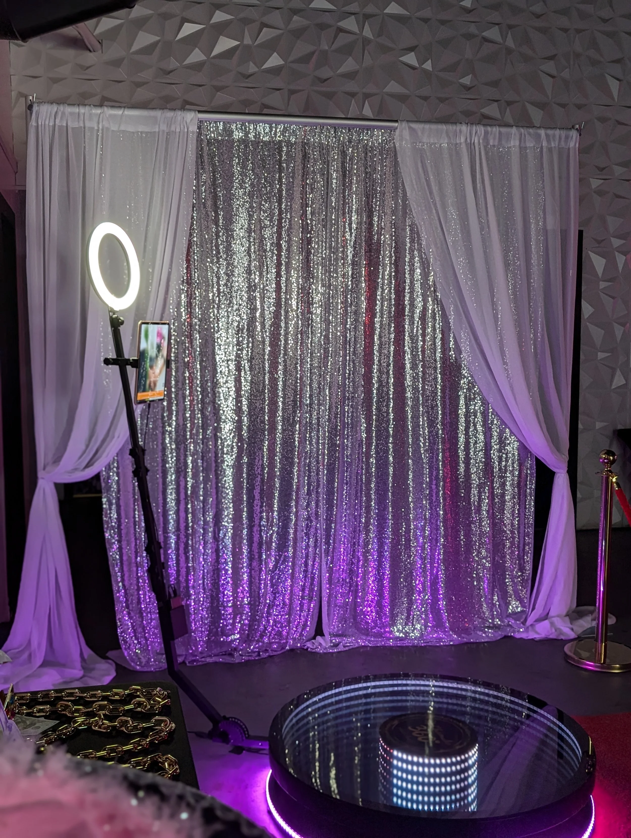 A wall with a large white rose flower design, a DJ equipment stand with a black turntable and people sign with social media icons, in a room with marble floor tiles.