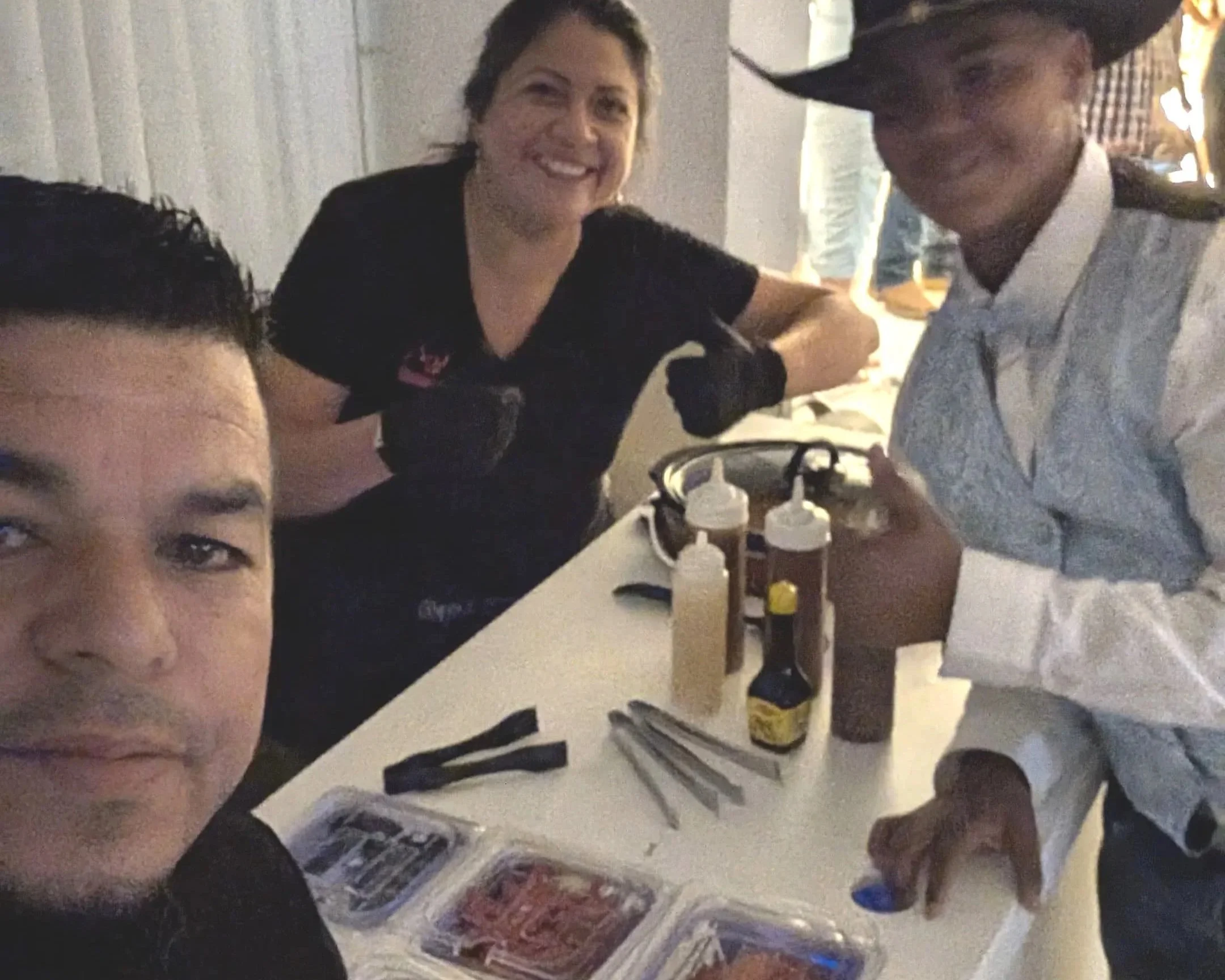 Outdoor event setup with a table covered by a white cloth lit with colorful lights, and a counter with a pyramid of pink boxes and a sign for "R&D Chamuko Events", featuring condiments, cups, and a hot beverage dispenser.