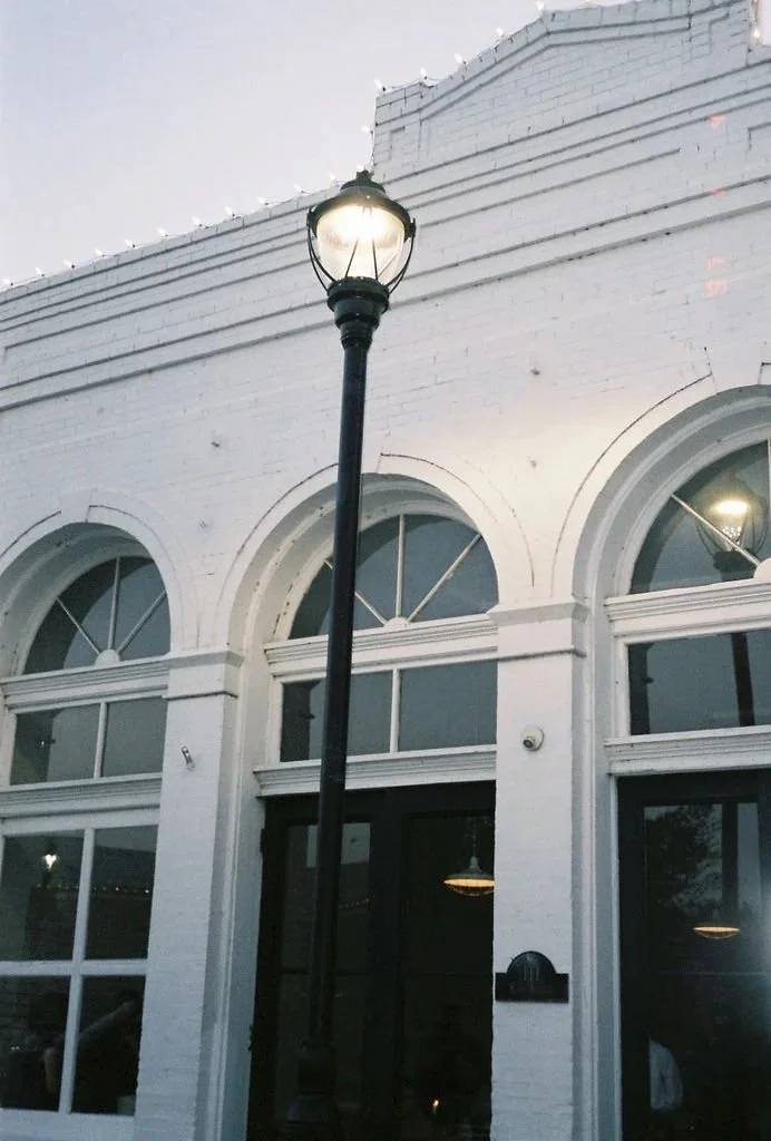 Outdoor scene with a black street lamp in front of a white brick building featuring large arched windows.