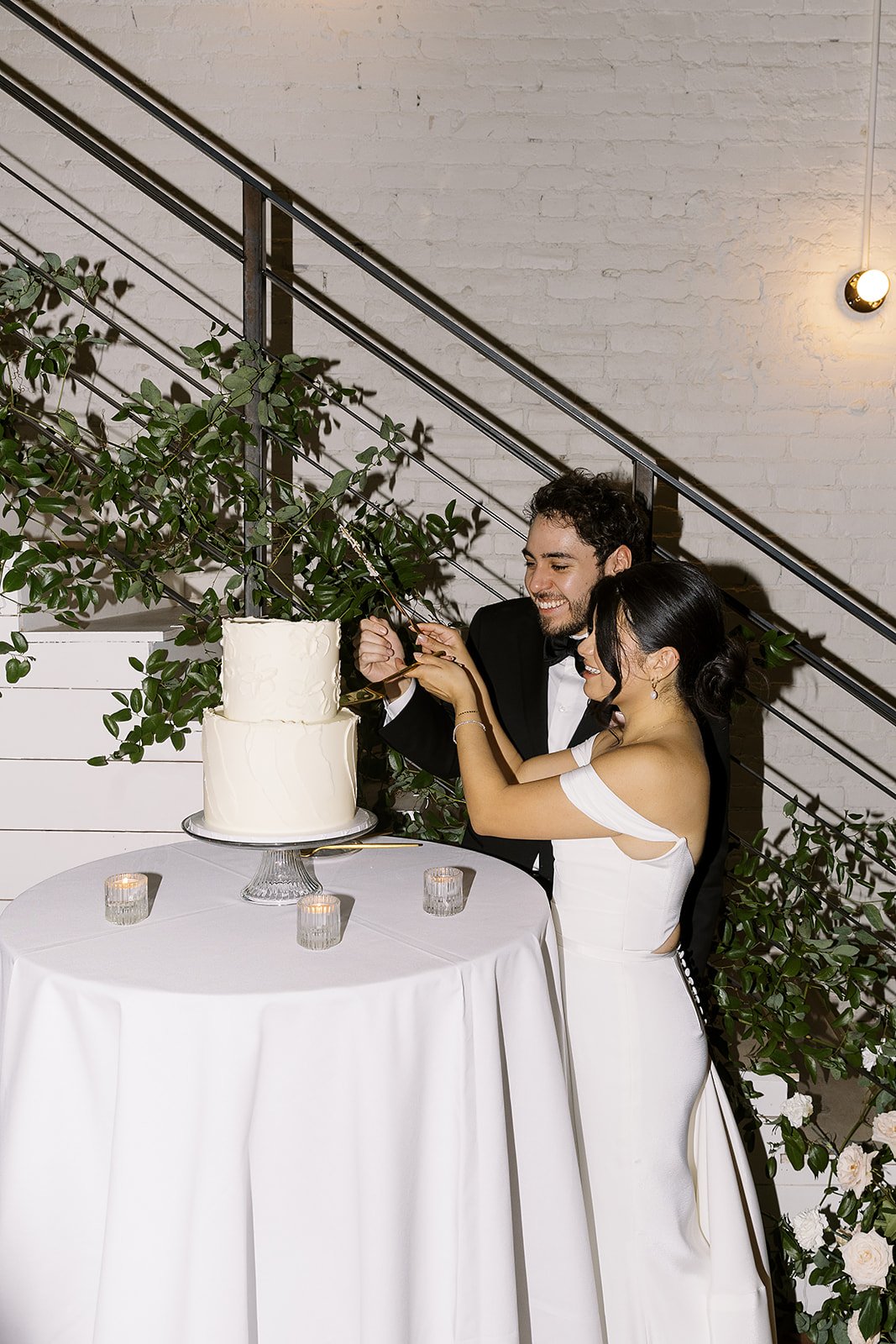 Newlywed couple cutting a wedding cake together at a wedding reception, smiling and celebrating.