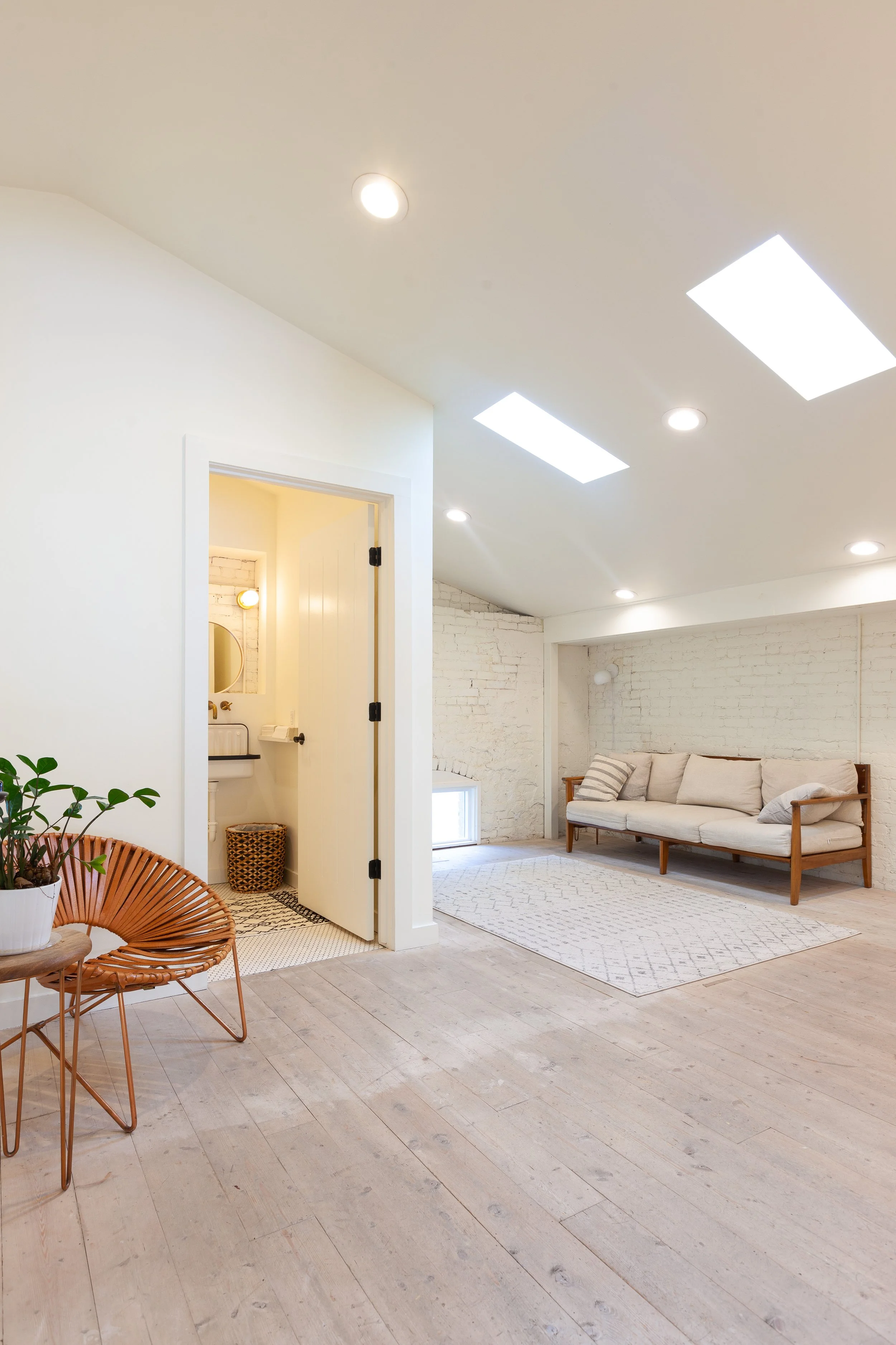 Bright living room with white brick wall, wooden sofa with cushions, lantern pendant, and skylights.