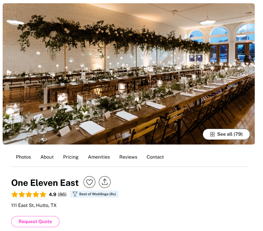 Elegant wedding reception setup in a spacious, well-lit room with large arched windows, a long wooden table decorated with greenery and candles, and a lush overhead floral arrangement.