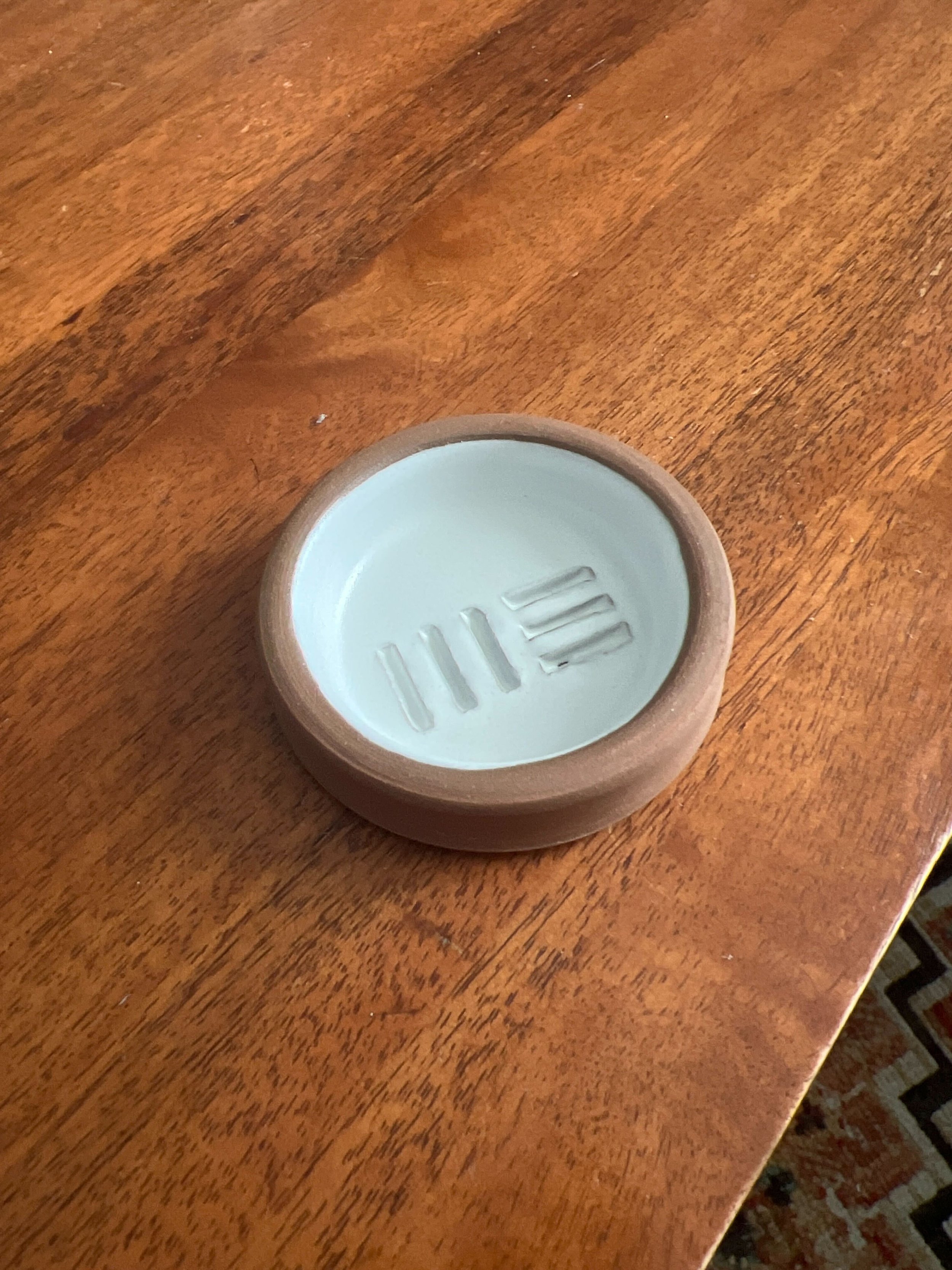 Small ceramic soap dish with three ridges for soap, placed on a wooden surface.