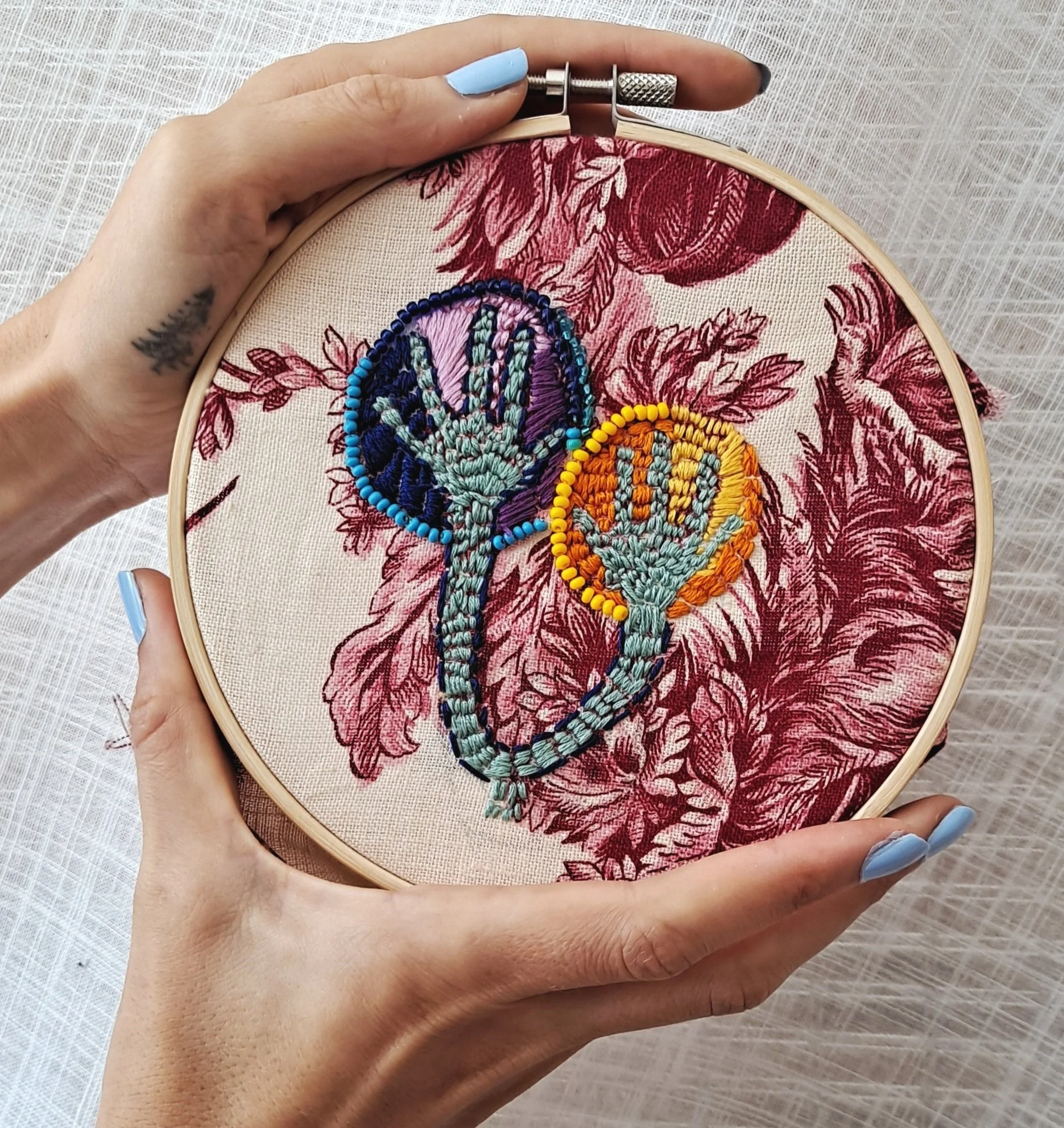 Embroidery artwork of colorful balloons with beaded outlines on a floral fabric background.