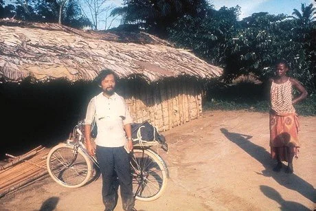 man standing with bicycle in front of a hut