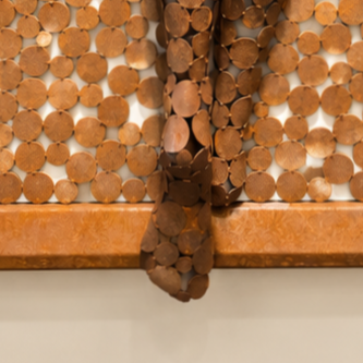 Gros plan sur une sculpture murale abstraite composée de pièces de monnaie cuivrées disposées en mosaïque.