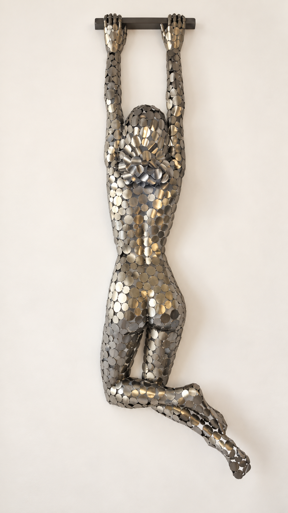Sculpture murale d’une femme nue en position assise, recouverte de pastilles métalliques argentées et dorées.