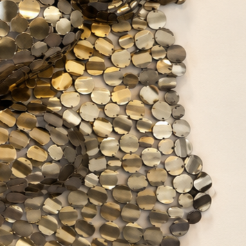 Gros plan d’une mosaïque texturée composée de petits galets métalliques dorés, argentés et gris.