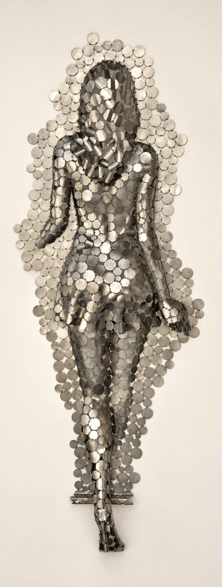 Sculpture murale abstraite en métal composée de centaines de pastilles métalliques circulaires, formant une silhouette allongée.