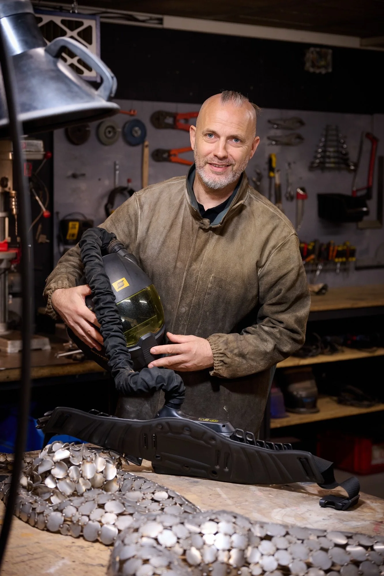 Un homme dans un atelier, tenant un casque de Soudure, entouré d'outils de bricolage et de pièces, prêt pour le travail.