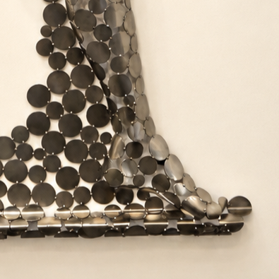 Détail d’un tissu métallique composé de disques sombres assemblés en angle, formant un motif triangulaire.