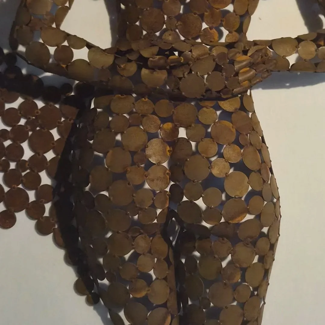 Gros plan d’une sculpture abstraite composée de nombreuses pièces métalliques rondes et brunes, éclairée sur un fond blanc.