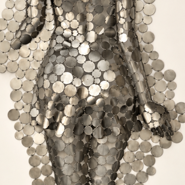 Gros plan d’une robe artistique composée de centaines de pastilles métalliques argentées reliées entre elles.
