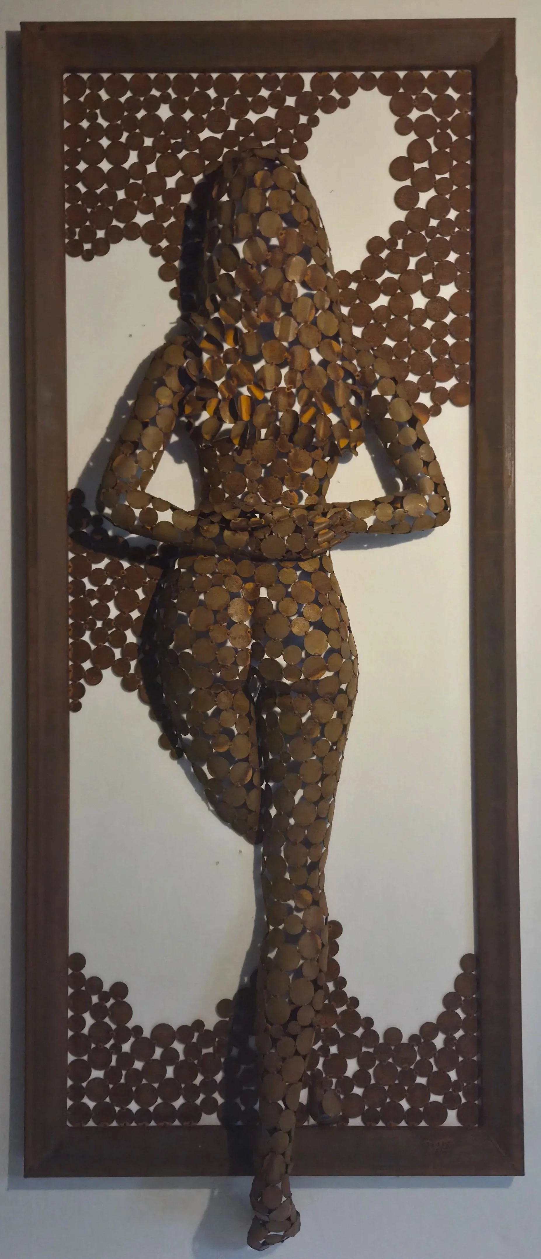 Sculpture murale représentant un personnage ailé, composée de pièces métalliques brunes dans un cadre en bois.
