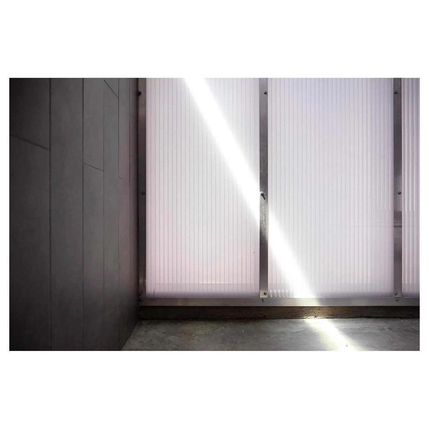 Close-up of a modern exterior wall with a metal door and vertical frosted glass panels, illuminated by sunlight.