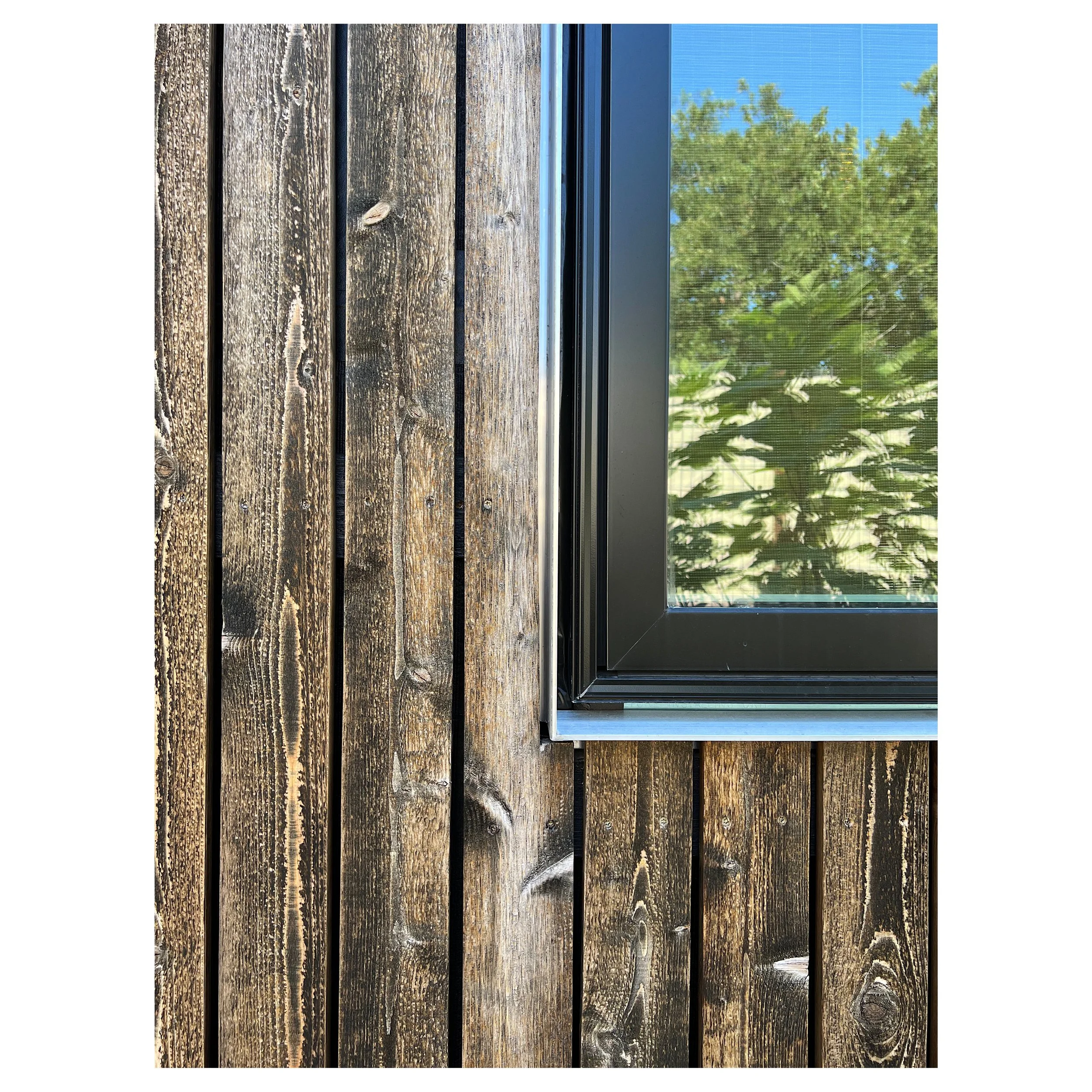 Close-up of a wooden exterior wall with dark brown stained, horizontal planks and a window with a black frame.