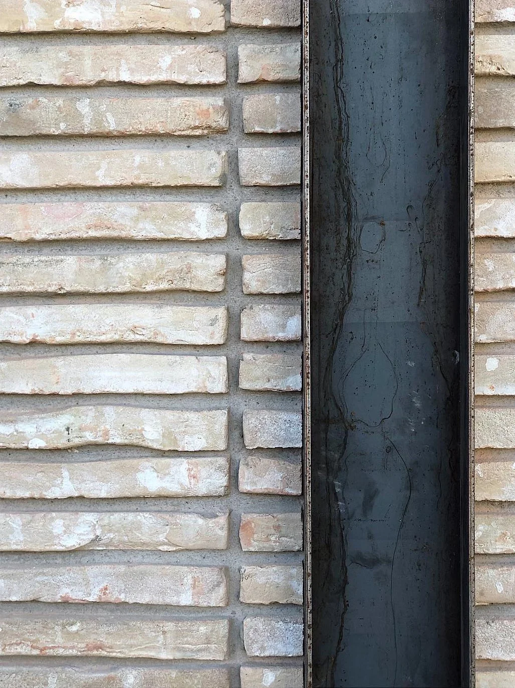 Close-up of a brick wall with a narrow dark metal vent or decorative panel in the center.