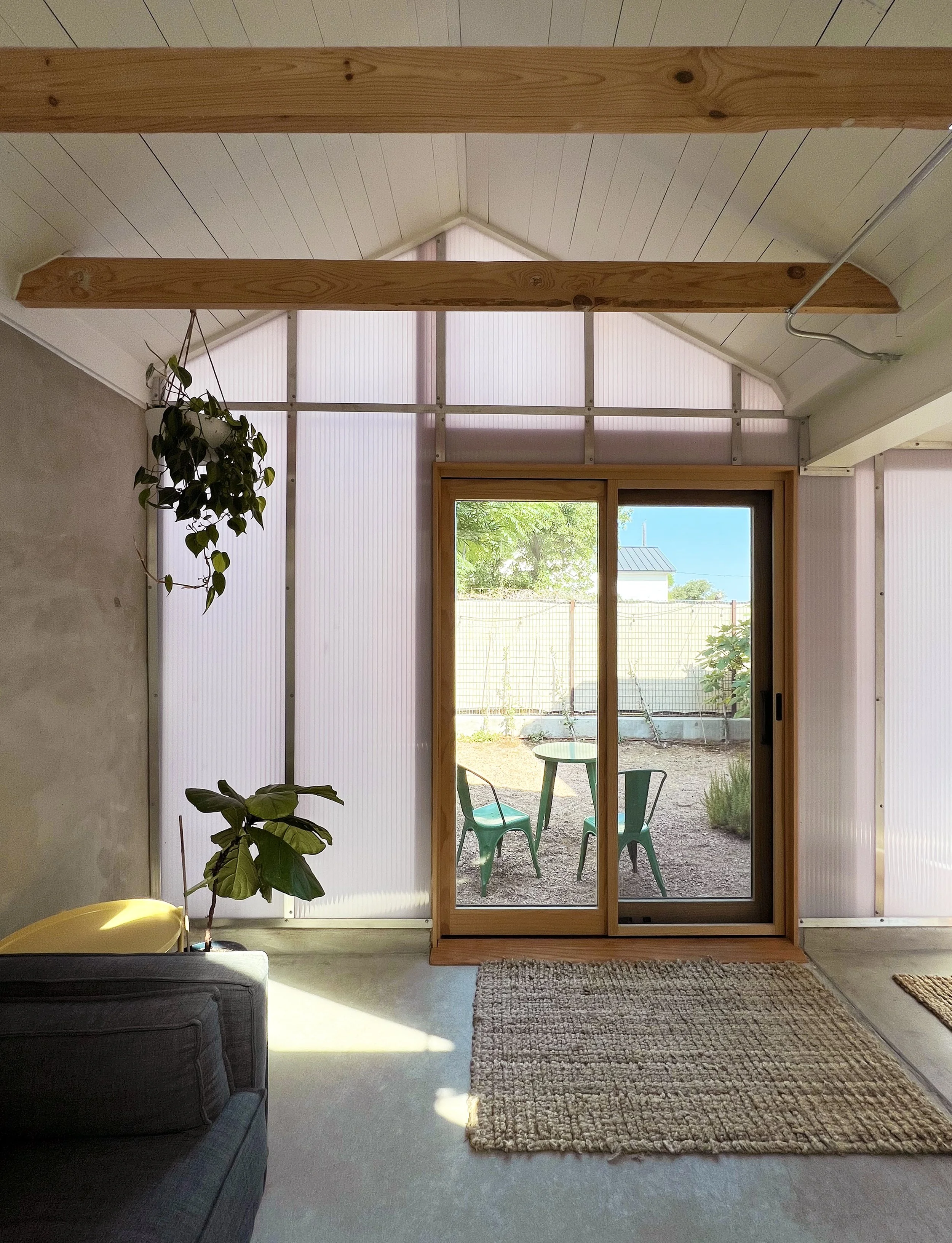Interior view of a room with a sliding glass door leading to an outdoor patio with a small table and two chairs, and visible garden area.