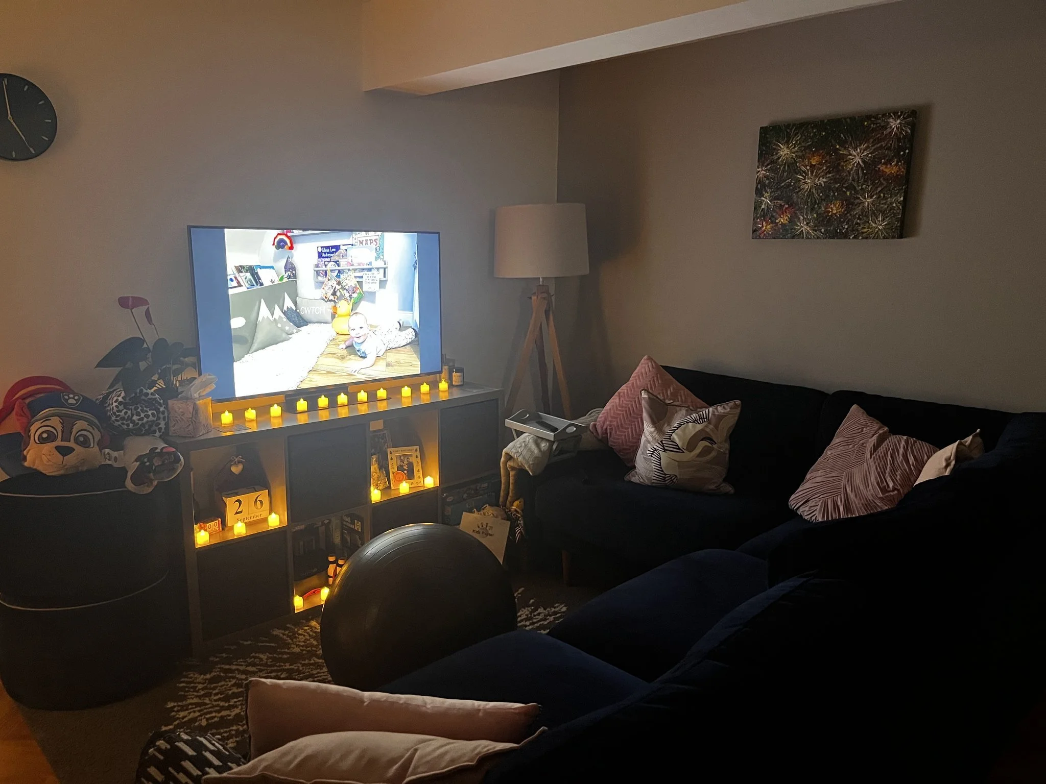 a tv is on with a photo of a baby on it. led candles are lit and there is a birth ball in front of a sofa