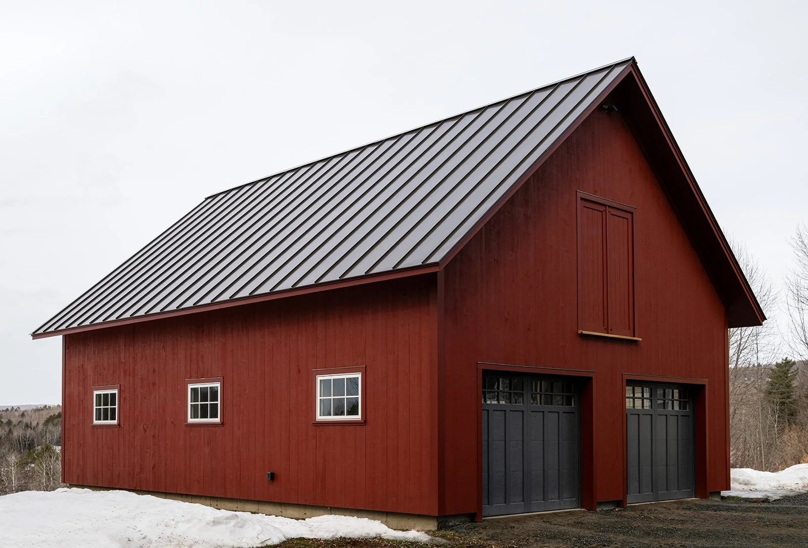 Facing the road, the two dark gray garage doors mimic old yankee barns, whose barn doors were on the gable ends. A loft door painted red to blend in with the facade is above the garage doors.