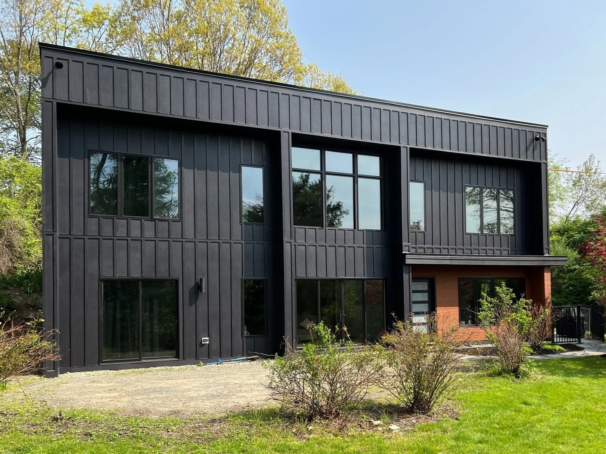 Exterior of a modern home in Westborough, MA, featuring black siding with sienna-colored wood around the entry on the lower right
